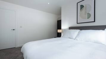 Una habitación de hotel moderna con una cama grande, una mesita de noche, una lámpara y una obra de arte enmarcada en la pared.