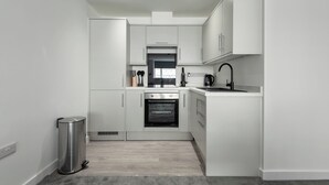 Eine moderne Küche mit weißen Schränken, einem Edelstahl-Mülleimer, einem eingebauten Backofen und einem schwarzen Wasserhahn.