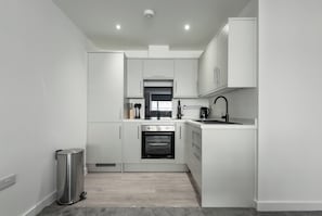 A modern kitchen with white cabinets, a stainless steel trash can, a built-in oven, and a black faucet.