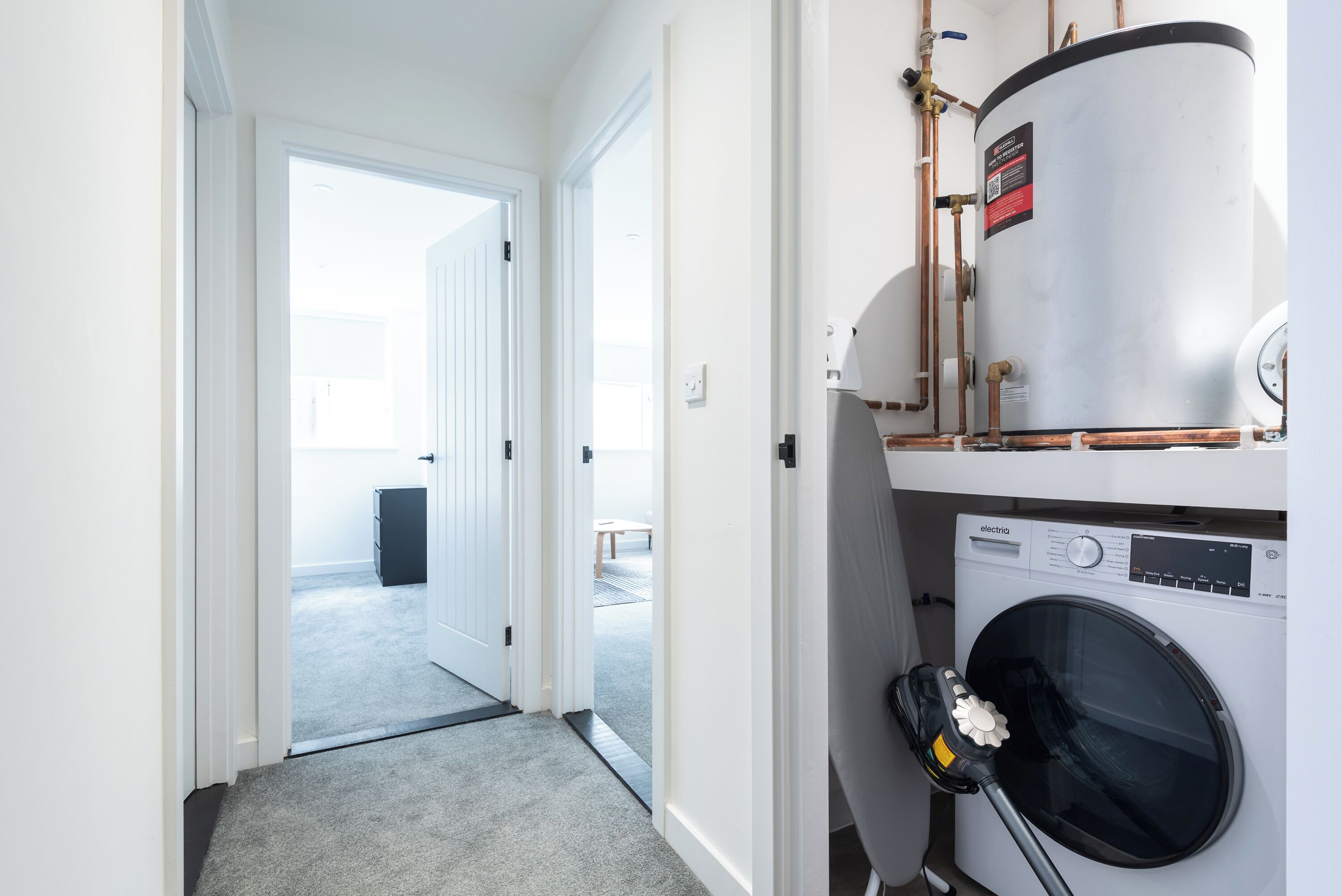 A laundry room with a washing machine, a water heater, and a vacuum cleaner.