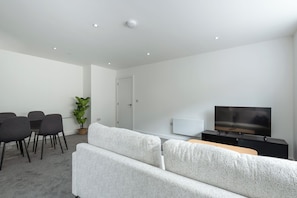 Un salon moderne avec un canapé, un téléviseur, une table à manger avec des chaises et une plante en pot.