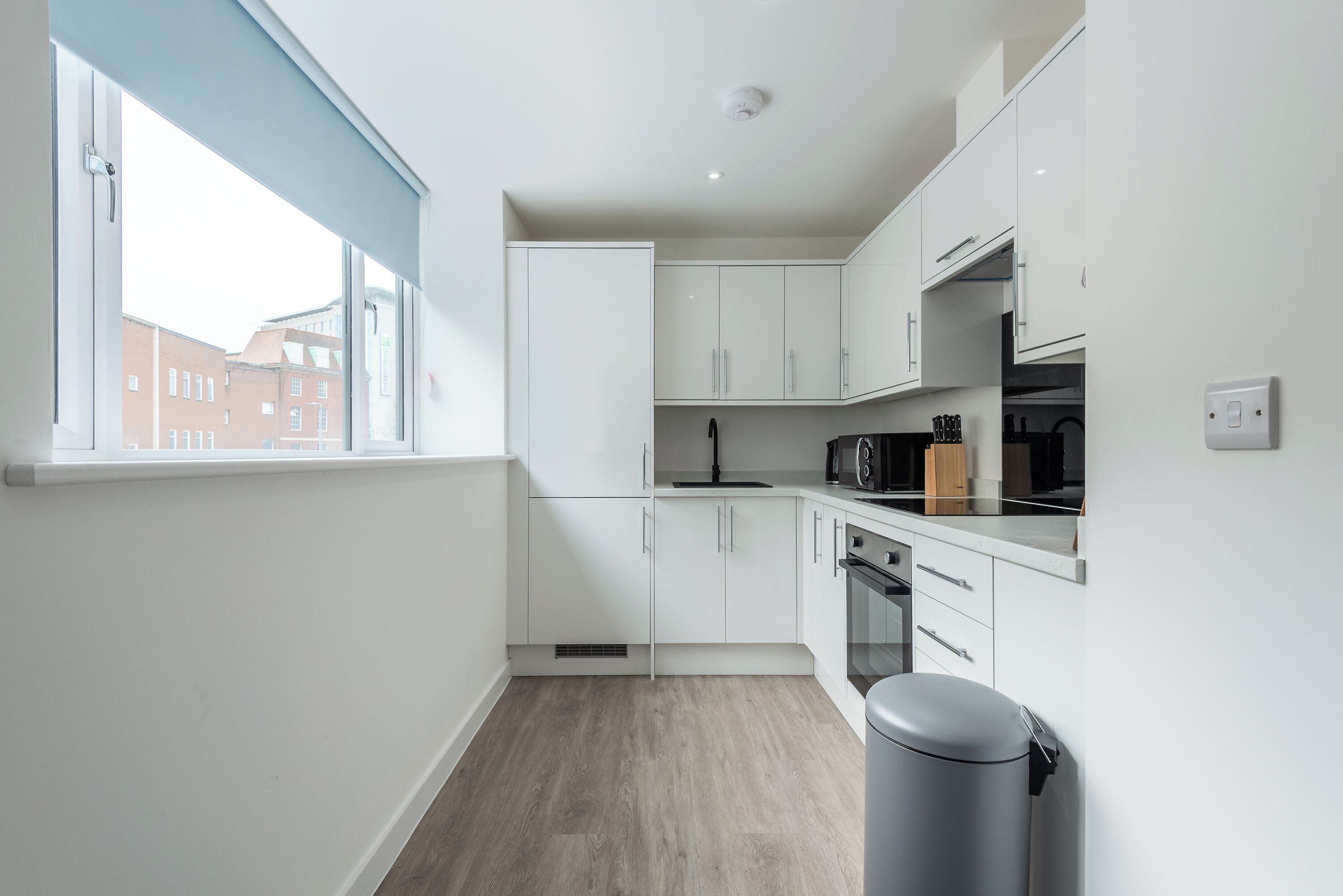 Una cocina moderna con armarios blancos, encimera negra y una ventana con vistas a edificios.
