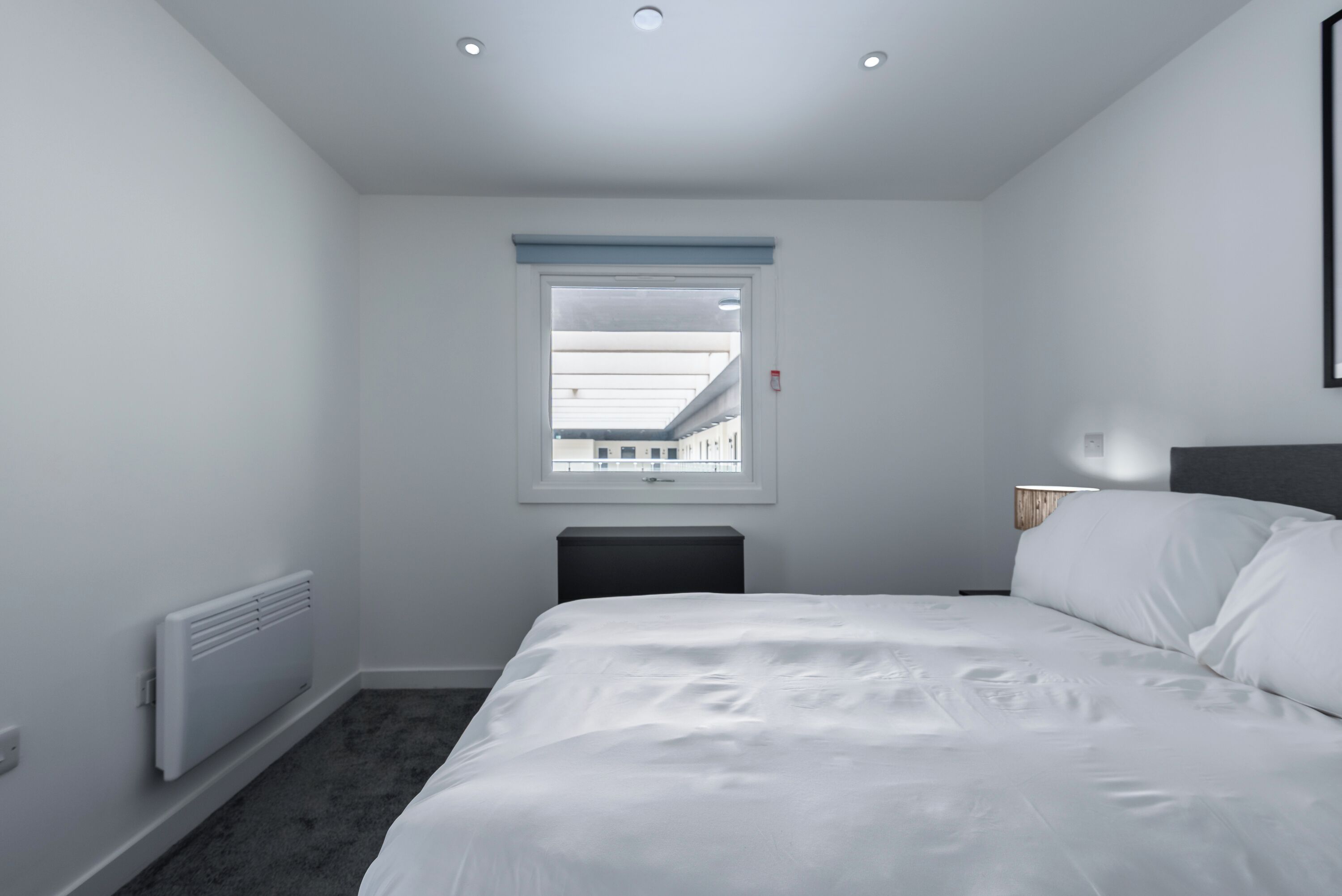A bedroom with a bed, a radiator, a window, and a bedside table.