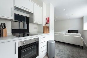 Une cuisine moderne avec des meubles blancs, un four encastré et une poubelle grise.