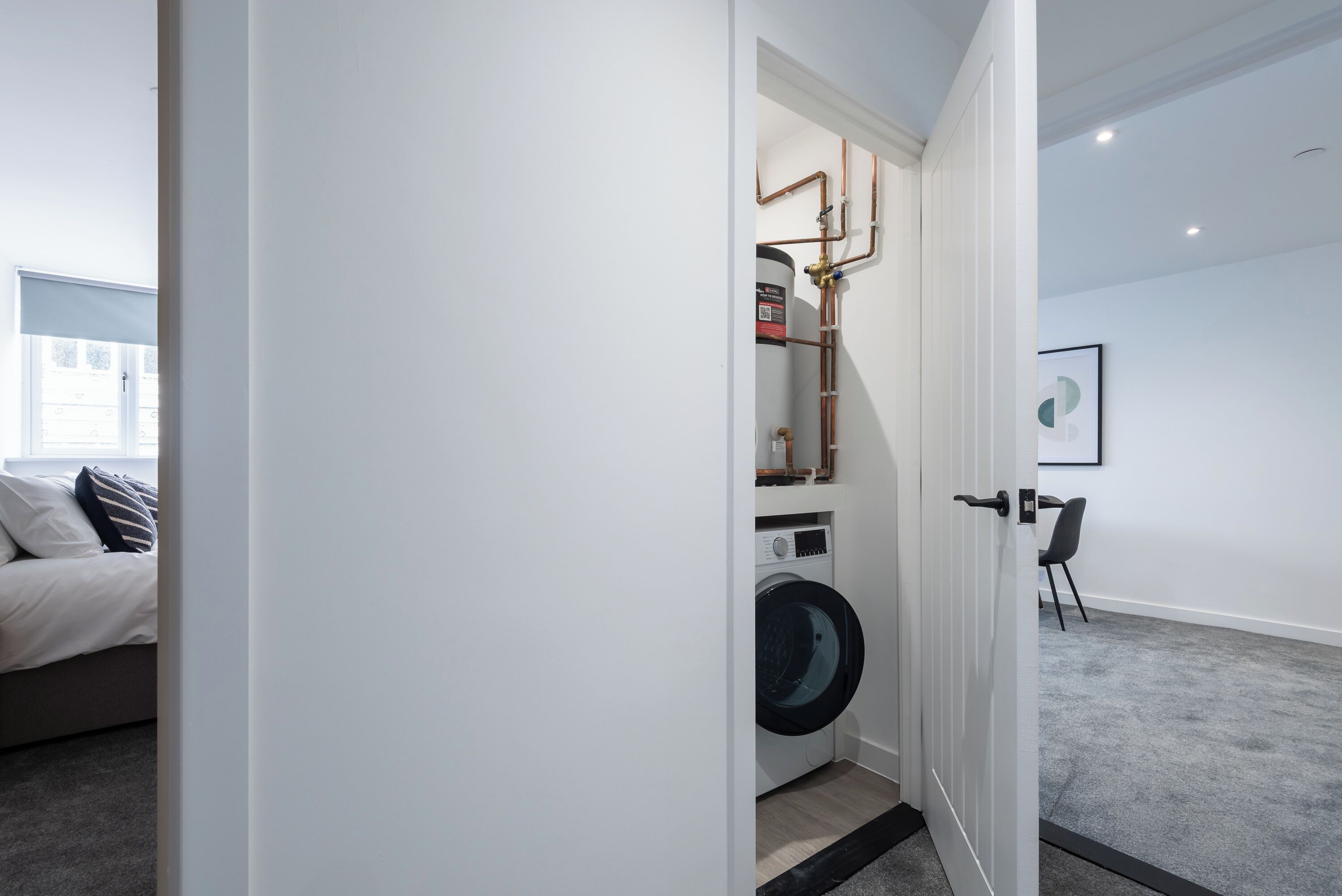 A modern laundry room with a washing machine, a water heater, and visible plumbing.