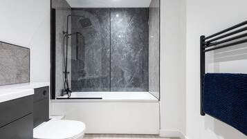 Un baño moderno con ducha envuelta en vidrio, inodoro blanco y bañera.
