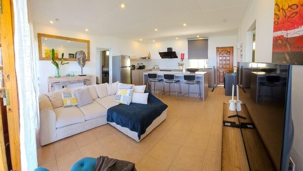 A spacious living area with a sofa, a dining table, and a kitchen in the background.