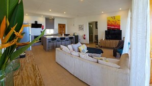 A modern living room with a sofa, a dining area with chairs, a kitchen, and a TV.
