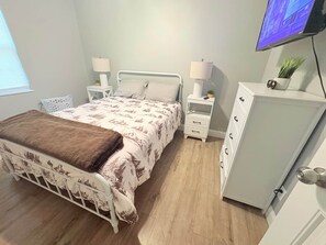 A bedroom with a bed, nightstands, a dresser, a television, and a window. - Nature's Nook I Cozy 2BR I 15m to RRG I Wi-Fi (Stanton)