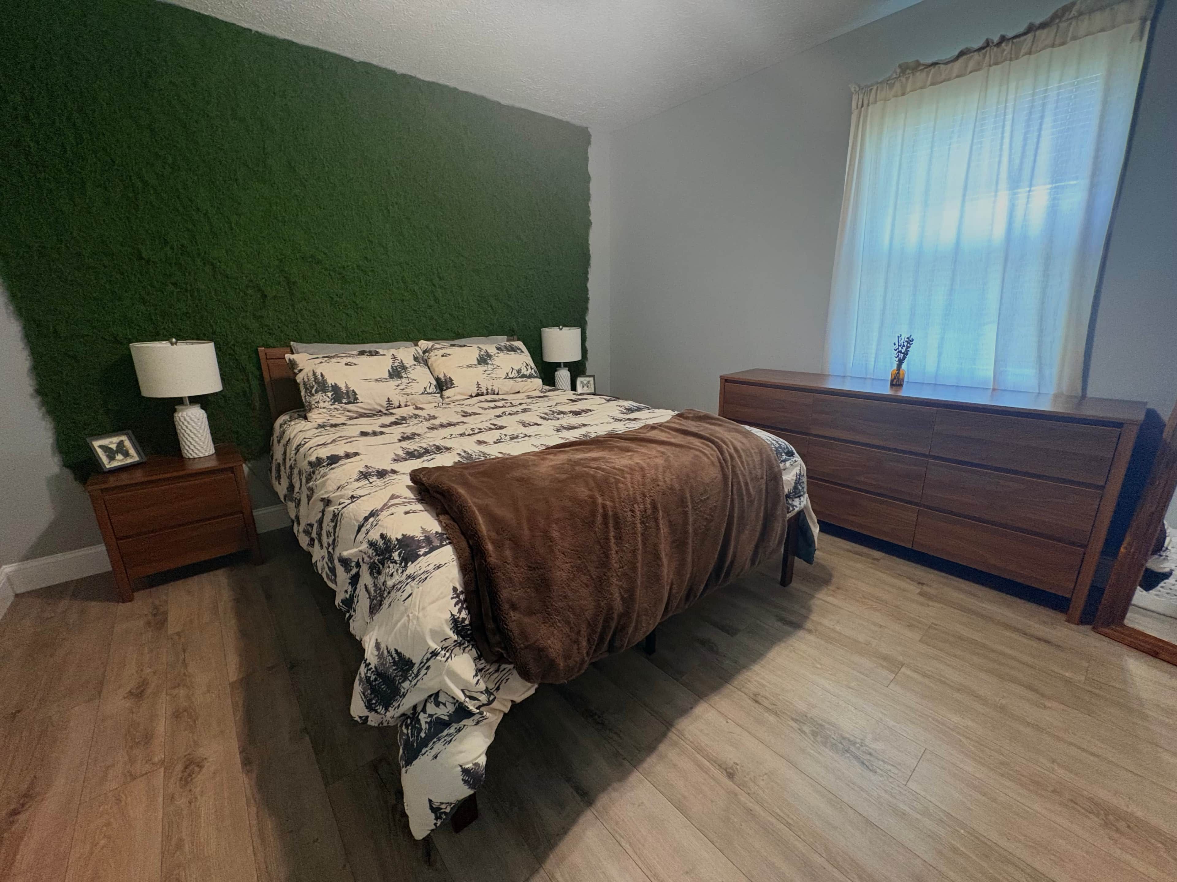 A bedroom with a bed, a dresser, a nightstand, and a green wall.