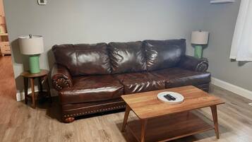 A brown leather sofa with decorative stitching, two side tables with lamps, and a wooden coffee table in a living room with light wooden flooring.