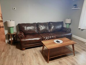 A brown leather sofa with decorative stitching, two side tables with lamps, and a wooden coffee table in a living room with light wooden flooring. - Nature's Nook I Cozy 2BR I 15m to RRG I Wi-Fi (Stanton)