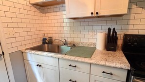 A compact kitchen with white cabinets, a stainless steel sink, and a black stove. - Nature's Nook I Cozy 2BR I 15m to RRG I Wi-Fi (Stanton)