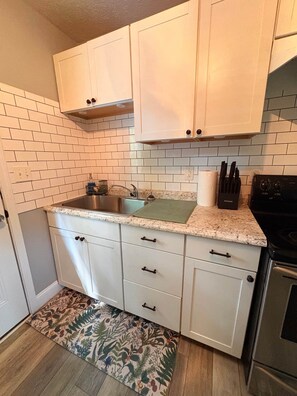 A compact kitchen with white cabinets, a stainless steel sink, and a black stove. - Nature's Nook I Cozy 2BR I 15m to RRG I Wi-Fi (Stanton)