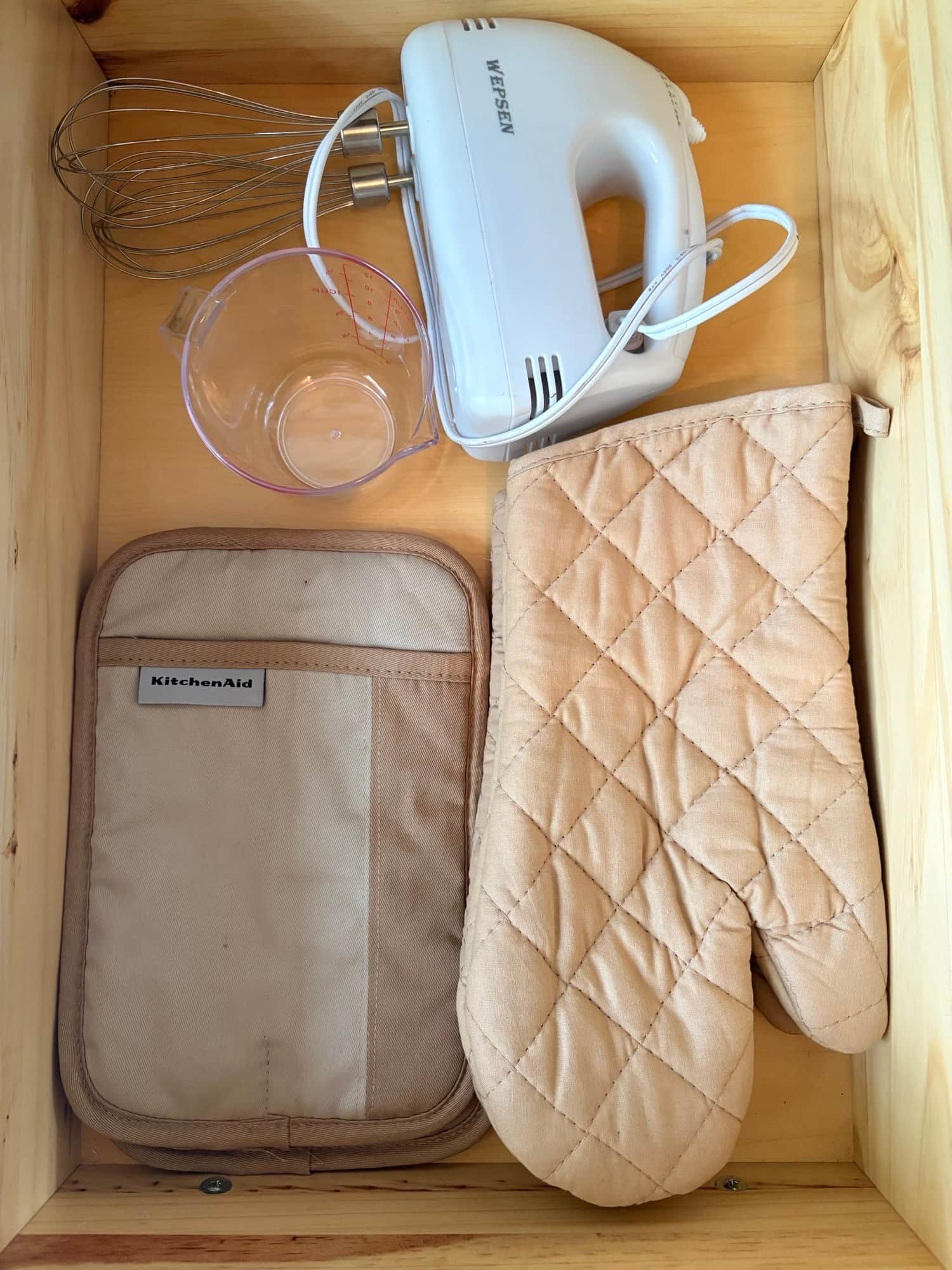 Eine Holzaufbewahrungsbox mit Küchengerät, Messbecher, Schneebesen und einer gesteppten Topflappen.