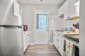 A kitchen with white cabinets, a microwave, a refrigerator, and a patterned shower curtain. - Nature's Nook I Cozy 2BR I 15m to RRG I Wi-Fi (Stanton)