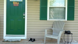 A green door with a welcome sign, a window with green shutters, a white chair, and a small table with a kettle and a pot. - Nature's Nook I Cozy 2BR I 15m to RRG I Wi-Fi (Stanton)