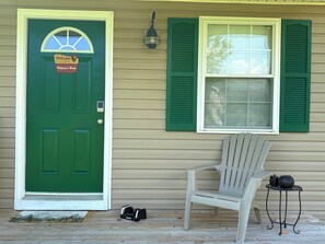 A green door with a welcome sign, a window with green shutters, a white chair, and a small table with a kettle and a pot. - Nature's Nook I Cozy 2BR I 15m to RRG I Wi-Fi (Stanton)