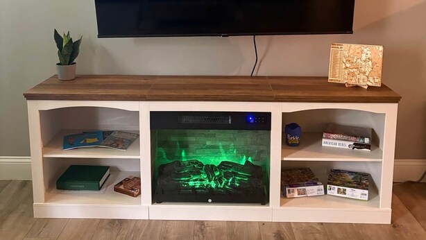 A flat-screen TV mounted on a wooden entertainment center with shelves below. - Nature's Nook I Cozy 2BR I 15m to RRG I Wi-Fi (Stanton)