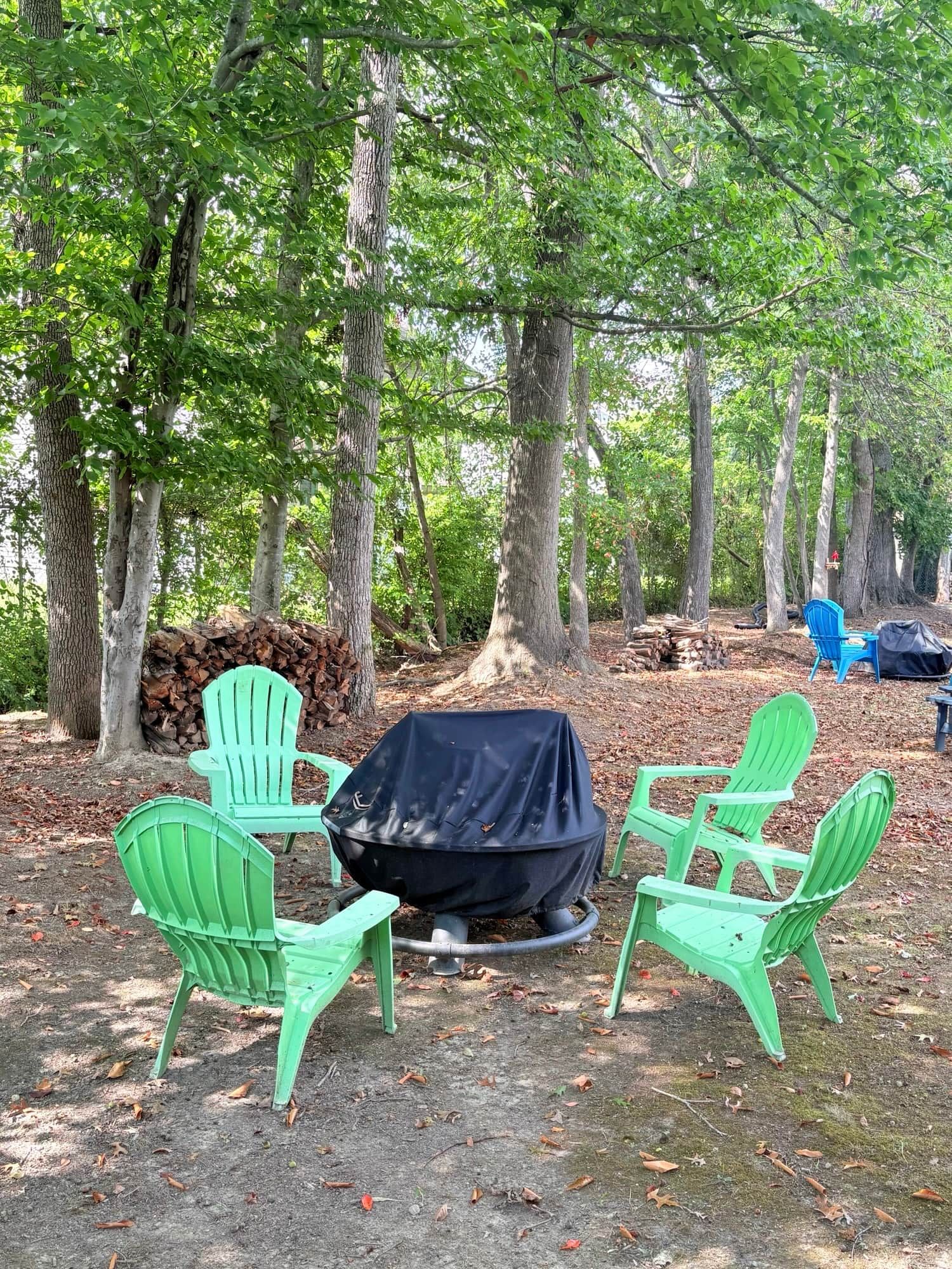 A campsite with green chairs around a covered grill, surrounded by trees.