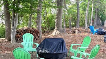 A campsite with green chairs around a covered grill, surrounded by trees.