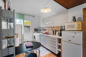 A compact kitchen with a dining area, a washing machine, a microwave, and a coffee maker. - Holiday Home "Sous les pins" with Private Garden, Wi-Fi and Air Conditioning (La Garde)
