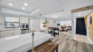 Uma cozinha moderna com armários brancos, uma ilha central e uma área de jantar com mesa e cadeiras.
