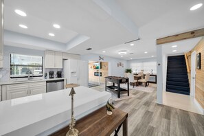 A modern kitchen with white cabinets, a central island, and a dining area with a table and chairs. - Waterfront Gulf-access home w/heated pool, boat lift, kayaks, & stunning sunsets (Cape Coral)