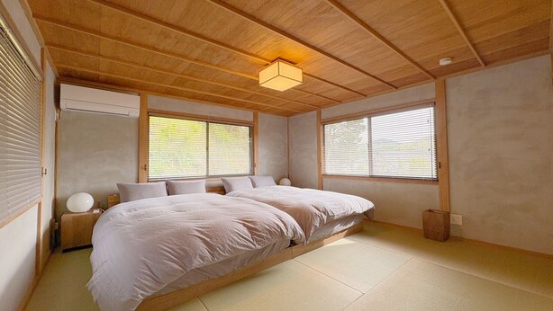 Une chambre dotée d’un grand lit, de poutres apparentes en bois au plafond et de fenêtres coulissantes.