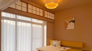 Une pièce avec une table en bois, un canapé jaune et une grande fenêtre ornée de rideaux légers.