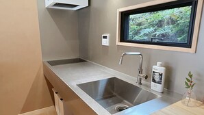Une cuisine moderne avec un évier en acier inoxydable, une fenêtre donnant sur un espace verdoyant et une petite plante en pot posée sur le plan de travail.