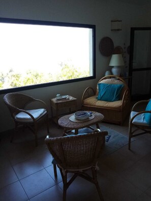 Una habitación con muebles de mimbre, un ventanal grande y una lámpara.