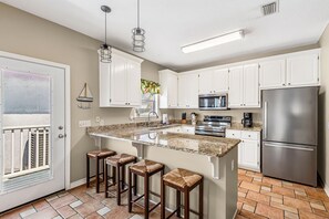 A kitchen with white cabinets, a stainless steel refrigerator, a granite countertop, and a bar stool. - 🔥 🏖️ Gone To The Beach: Firepit, Community Pool + Steps to Navarre Beach! (Navarre Beach)