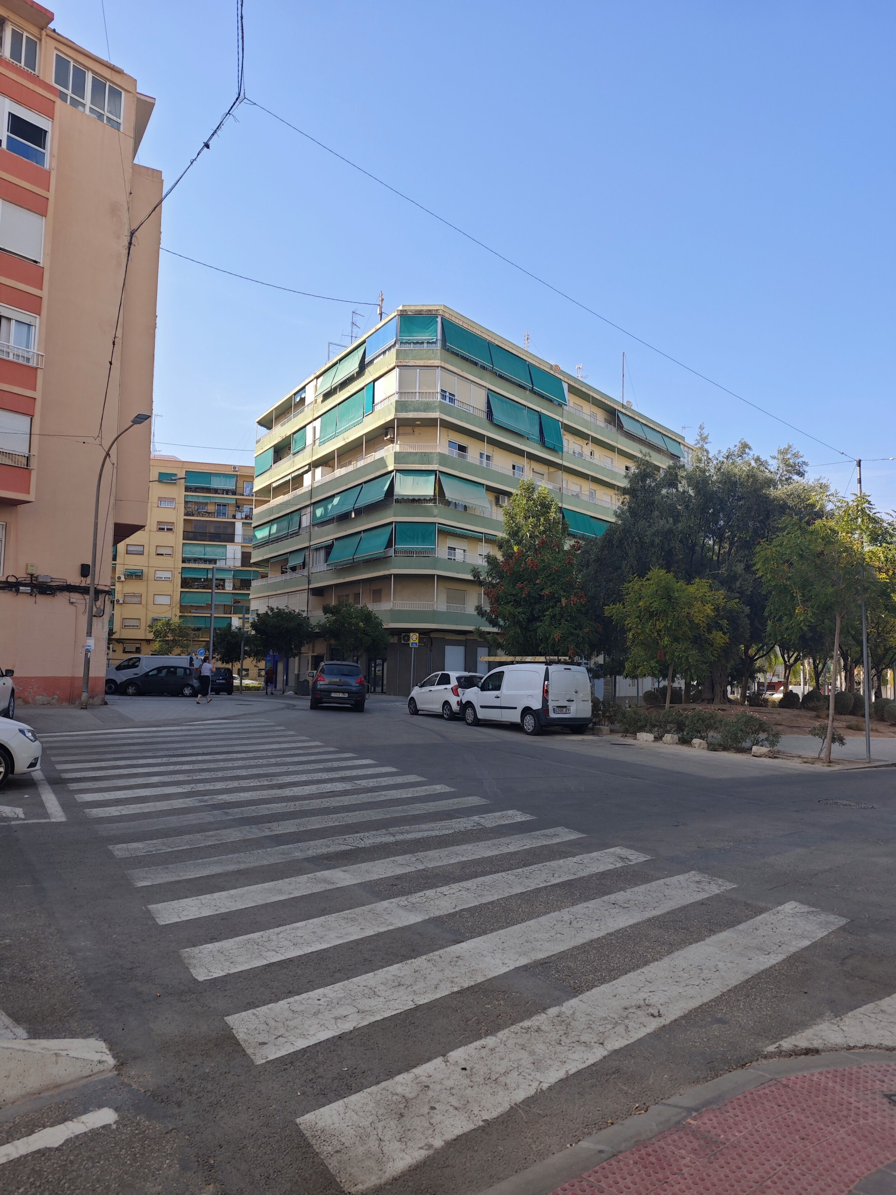 Un edificio de varios pisos con balcones, un paso de peatones y automóviles estacionados.