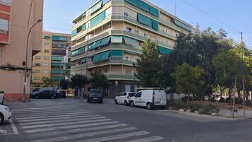Un edificio de varios pisos con balcones, un paso de peatones y automóviles estacionados.