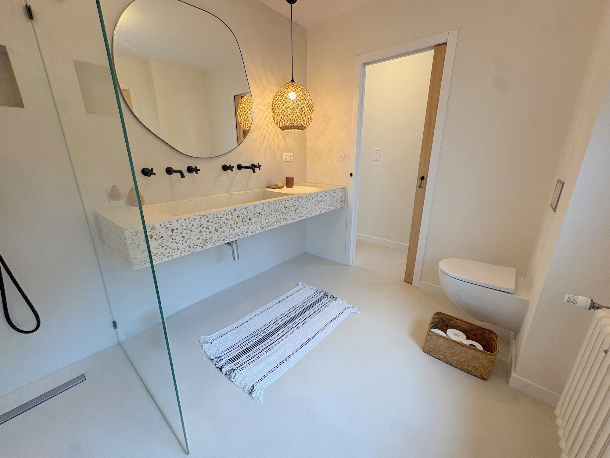 Une salle de bain moderne avec une douche à parois de verre, un lavabo sur pied et un miroir rond.