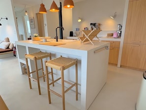 Eine moderne Küche mit Kochinsel, Barhocker, Pendelleuchten und Holzschnitzereien.