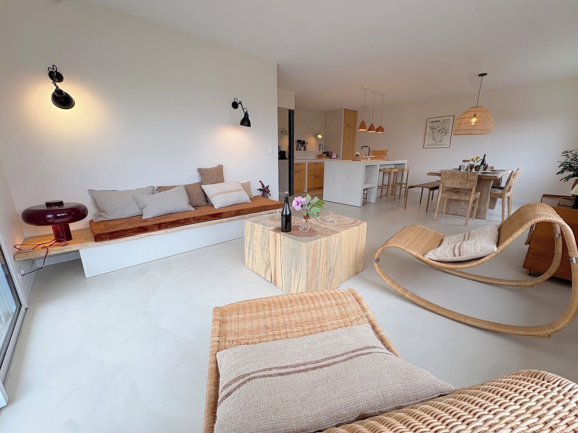 Un salon moderne avec un canapé, une table basse en bois, des chaises en osier et, au fond, un coin repas.