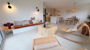 Ein modernes Wohnzimmer mit einer Couch, einem Holztisch, Korbstühlen und einem Essbereich im Hintergrund.