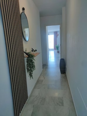 Ein Flur mit gestreifter Wand, einem Spiegel, einem Pflanzenregal und einer großen Vase.