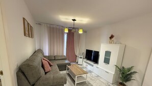 A living room with a sectional sofa, a TV, a small table, and a potted plant. - La cala "Tourism & Holidays" Swimming Pool & Parking (La Cala del Moral)