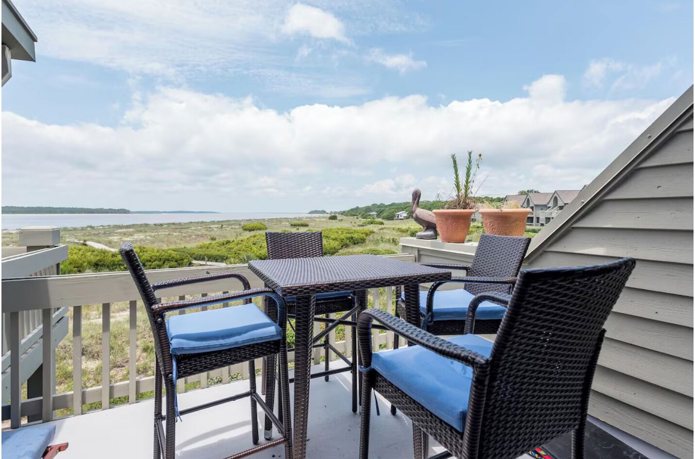 A balcony with wicker furniture and potted plants, overlooking a coastal landscape.