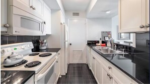 A compact kitchen with white cabinets, a stove, a microwave, and a refrigerator.