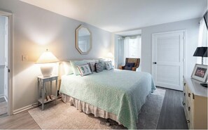 Une chambre à coucher comprenant un lit, des tables de chevet, un miroir, une chaise et une armoire.