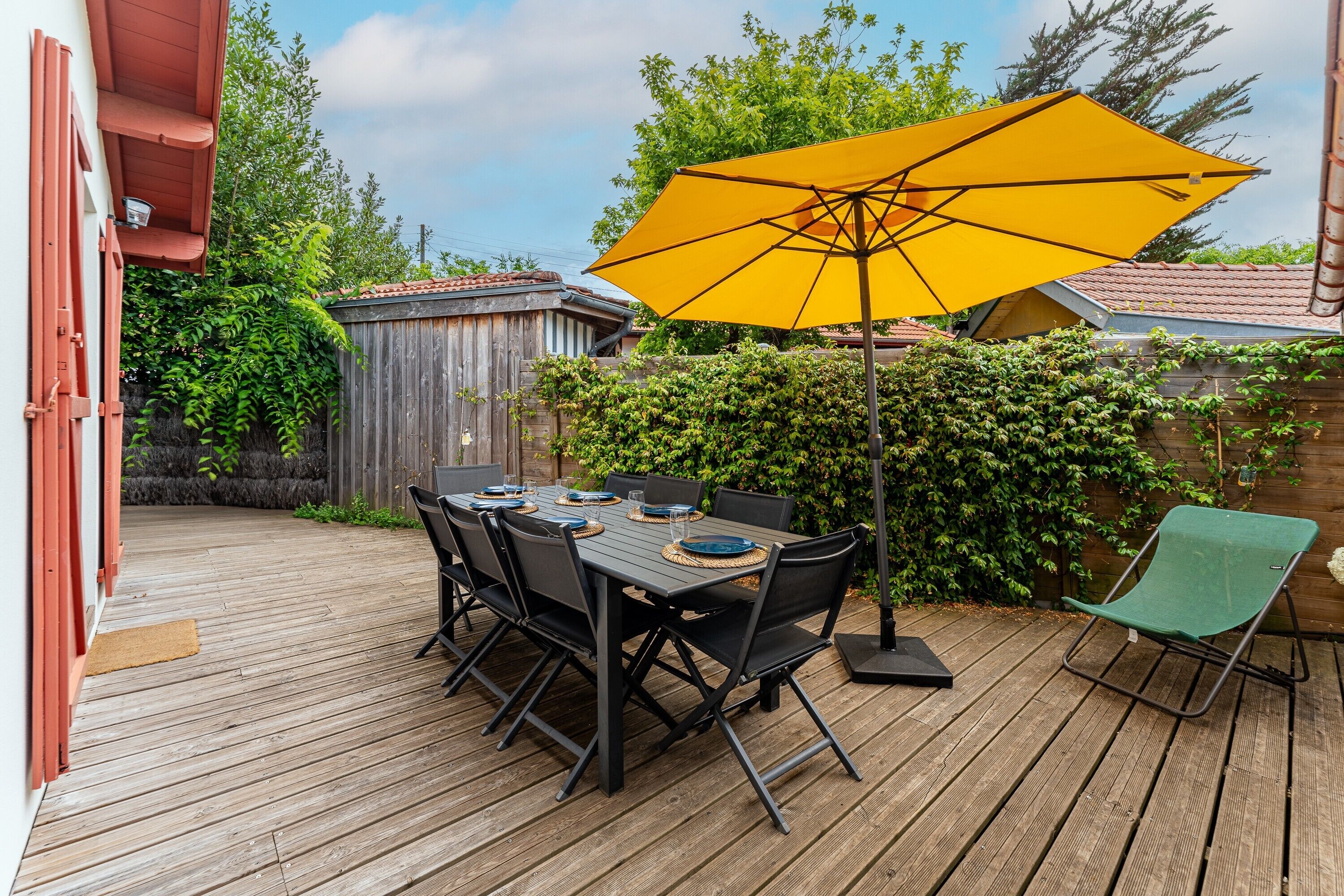 Una terraza de madera con una mesa, sillas, un paraguas amarillo y una silla verde.