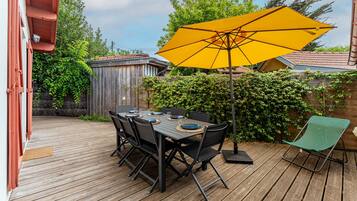 Una terraza de madera con una mesa, sillas, un paraguas amarillo y una silla verde.