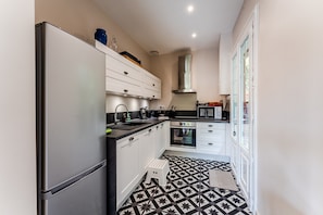 A compact kitchen with a refrigerator, oven, microwave, and white cabinetry. - Holiday Home “Villa Les Arbousiers Moulleau 300 m” with Terrace, Private Garden & Wi-Fi (Arcachon)