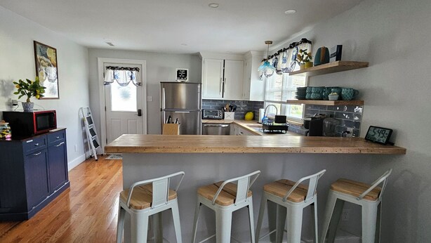 A modern kitchen with a central island, bar stools, a refrigerator, and a microwave. -  Charming 3 bed/2 bath house in Rock Hall with a 3-min walk to restaurants/town. (Rock Hall)
