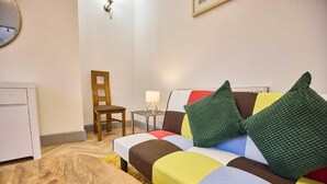 A small, neatly arranged room with a sofa, a chair, a small table with a lamp, and a radiator. - 1 Bed Flat - Sleeps 2 - Parking - Wifi (Nottingham)