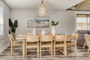 Ruokailutila, jossa on puinen pöytä ja tuolit, riippuvalaisin ja seinällä taulu.